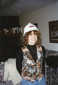 A picture of me in a hardhat from my first employer. Ignore the mom jeans and cat vest. It was 1996